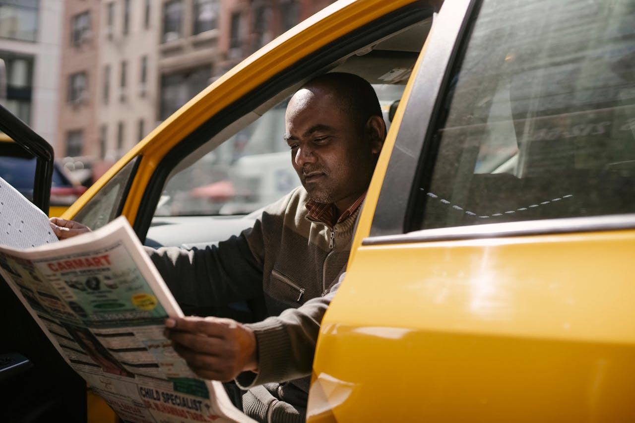 our-experience Concentrated male driver in casual clothes sitting in taxi during break and reading newspaper