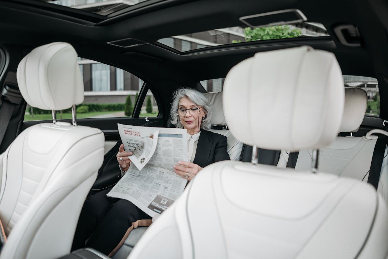 about-img Elderly woman in car reading a newspaper, showcasing a moment of relaxation and focus.
